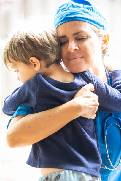성숙한 헬스케어 노동자는 전염병을 싸우기 위하여 병원에 가기 전에 그녀의 아들을 껴안고 포즈를 취합니다 - embracing smiling gap children only 뉴스 사진 이미지