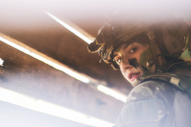 close-up vista através de buraco de parede de madeira de bela soldado mulher com traje de combate olhar para a câmera - equipped - fotografias e filmes do acervo