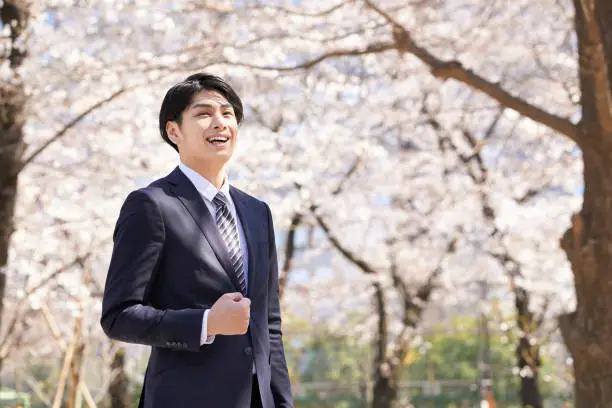 A smiling Japanese businessman stands with a cherry blossom in the background.