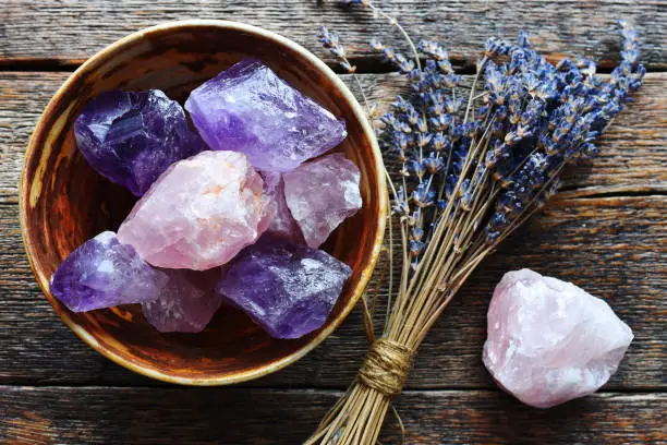 A table top image of a pottery bowl with large rose quartz and amethyst crystal with dried lavender flowers.