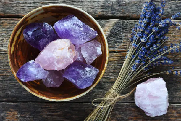 A table top image of a pottery bowl with large rose quartz and amethyst crystal with dried lavender flowers.