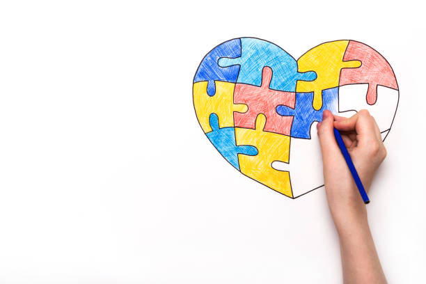 istock World Autism Awareness day. Children's hand draws heart from multi-colored puzzles. Mental health care concept 1215845183