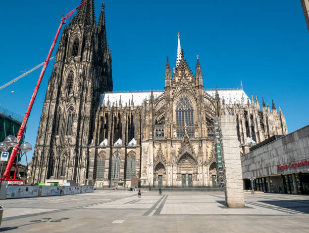 Cologne, Germany - June 15, 2025: Ornate facade of Cologne Cathedral featuring intricate stone work and large stained glass windows beneath a moody, overcast sky.