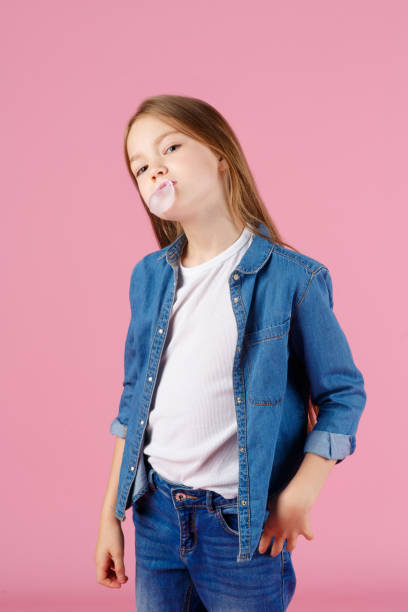 маленькая девочка в солнцезащитных очках взрывает розовую жевательную резинку на светло-фиолетовом фоне - chewing gum bubble blowing little girls стоковые фото и изображения