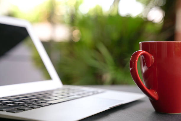 istock Computer laptop with red coffee cup. Garden background. 1215854059