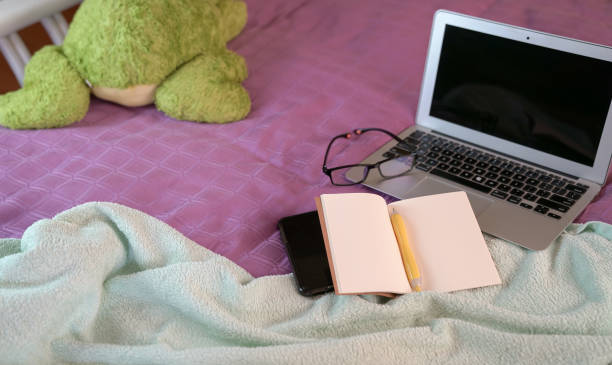 istock Computer laptop, notepad, cellphone on top of bed. Work from home. 1215854071