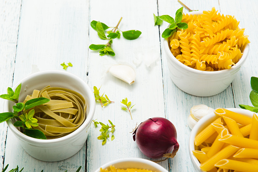 uncooked pasta variations and fresh spices on white wooden table