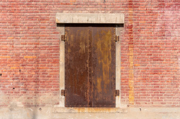 Old weathered rusty factory gate and the dated brown brick wall in the sunlight