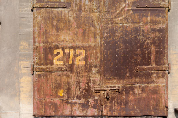 istock Old weathered rusty factory gate with number and the dated brown brick wall 1215855346