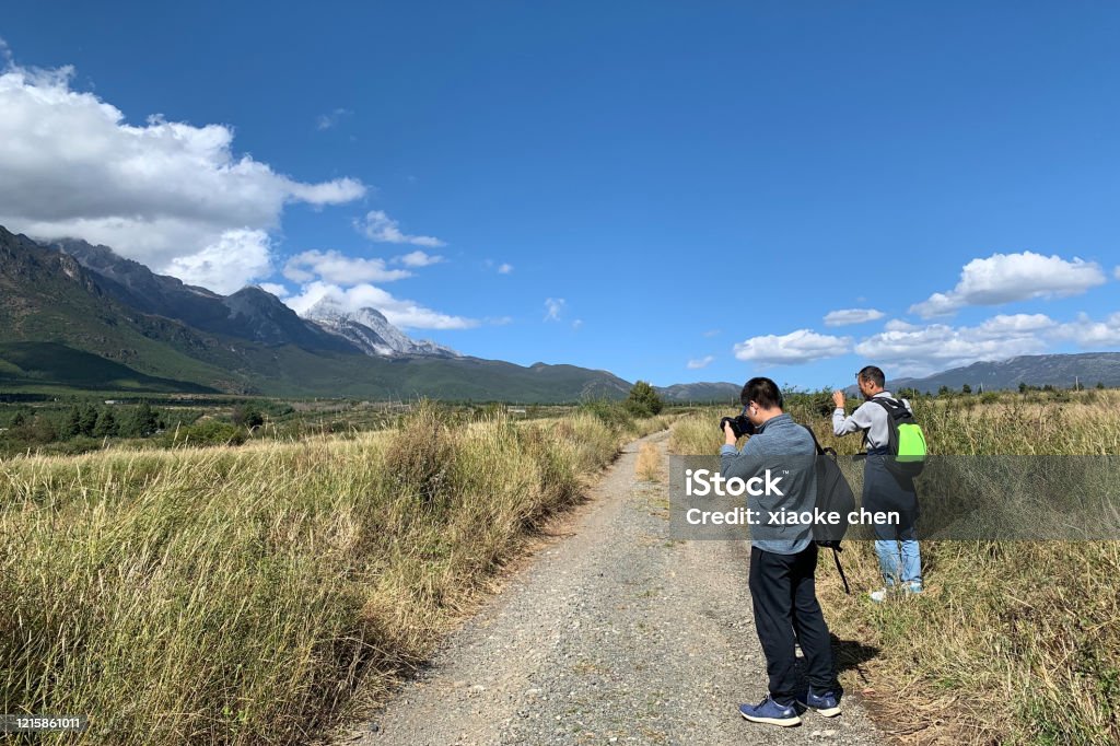 Two people were taking pictures on the road under the snow mountain Active Lifestyle Stock Photo