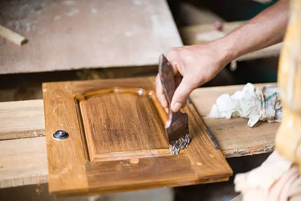 Photo of Man in workroom paints varnish on a piece of wood