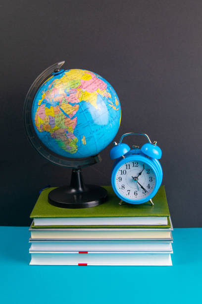 istock The globe and clock stand on a stack of books, on a blue table 1215863194
