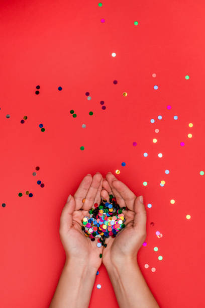 istock Multicolored confetti sparkles in female hands on a red background. Christmas concept. Background. 1215863586