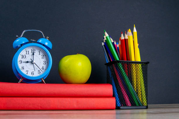 istock The blue alarm clock along with multi-colored pencils stand on a stack of red books, next to an apple 1215864600