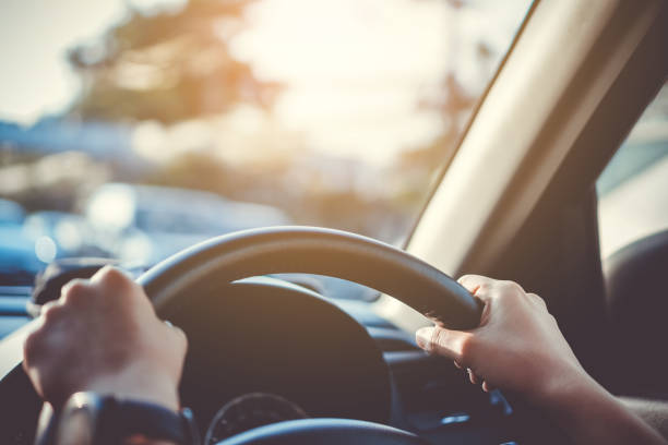 mano de mujer en el volante conducir un coche con fondo de luz solar. - conducir fotografías e imágenes de stock