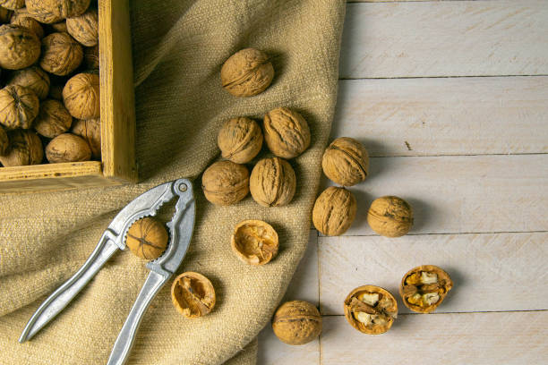 istock Walnuts in a wooden box, which stands on an old rustic sack, also scattered on a white table nearby is a cracker of walnut 1215865097