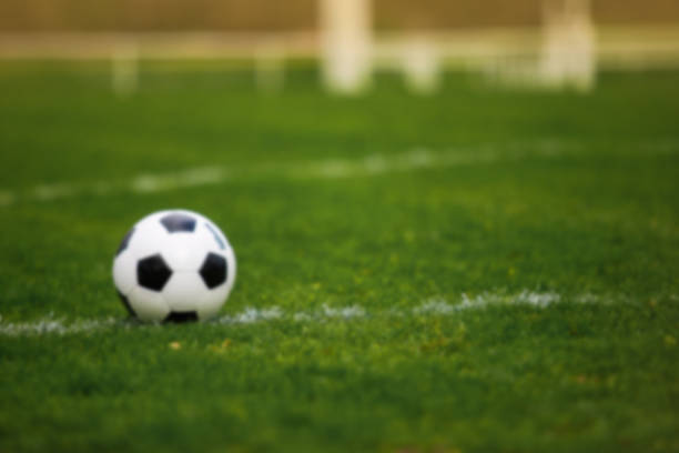 istock Blurred background of a Classic soccer ball, typical black and white pattern, placed on the white marking line of the stadium turf. Traditional football ball on the green grass lawn with copy space. 1215865971