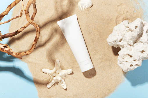 White bottle with skincare product. Summer decorations on sand. Starfish and seashell around cosmetology tube. Mockup style. Wellness and beauty concept