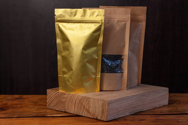 木製の背景に白い織物が付いている籐のバスケットにコーヒー豆と茶葉が入った茶色のクラフト紙のポーチバッグ。 - 5902 ストックフォトと画像