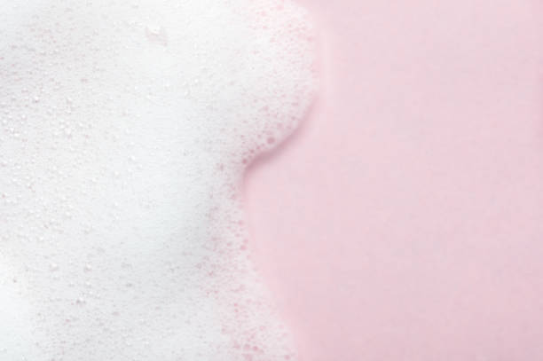 Foaming liquid on pink backdrop. Cosmetics foam background with copy space in right side. Cosmetic product sample of mousse, shampoo or soap. Skincare, cosmetology and beauty concept