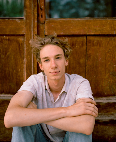 Portrait of a beautiful blond teenage boy sitting outdoors