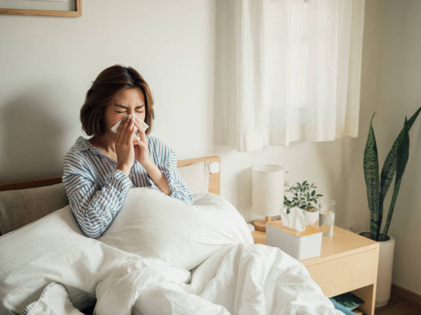 азиатская женщина получила чихание гриппа в ткани сидеть на кровати - cold and flu flu virus sneezing illness стоковые фото и изображения