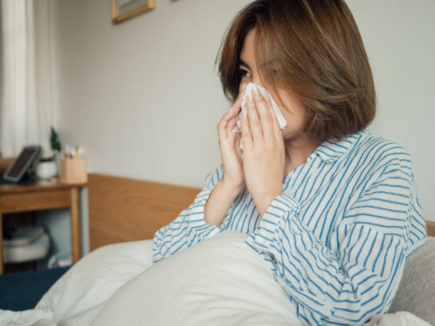 istock Asian woman got flu sneezing in tissue sit on bed 1215885737