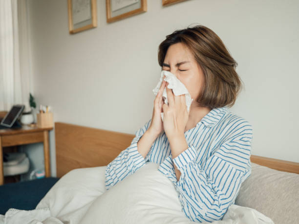 istock Asian woman got flu sneezing in tissue sit on bed 1215885768