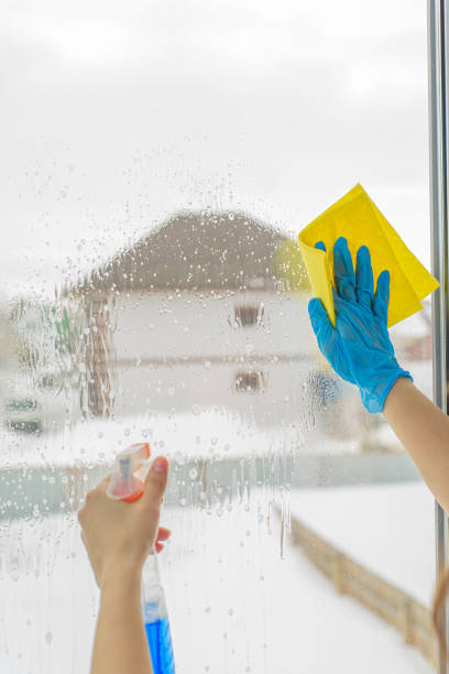 istock Hands in the blue gloves wash window with spray 1215888551