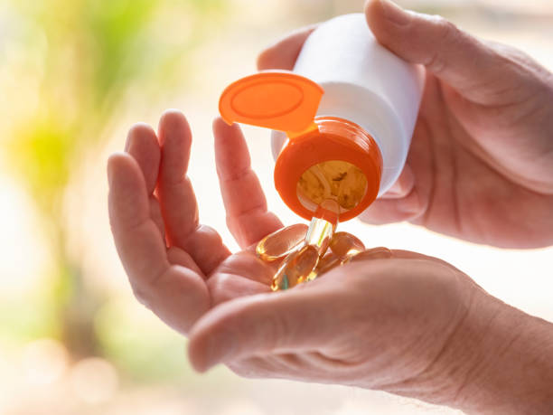 capsules de supplément nutritionnel étant placées d’une bouteille de médicament dans la paume de la main d’un homme. - vitamin pill flash photos et images de collection