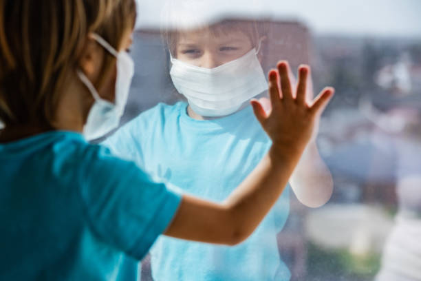 istock Reflection in a window of a sad boy with face mask in a quarantine. 1215889091