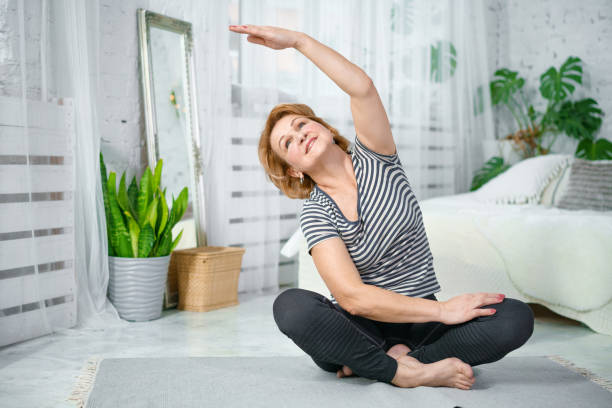 seniorin beim training im lotus. aktive reife frau, die dehnübungen im wohnzimmer zu hause macht. - core strength stock-fotos und bilder