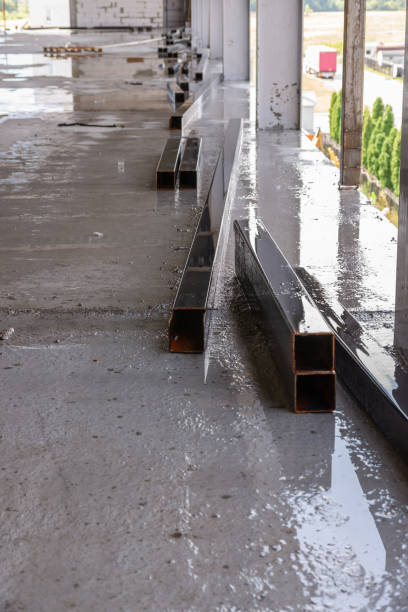 istock Big square metal pipes parts under rain on construction with sky in reflection. 1215897615