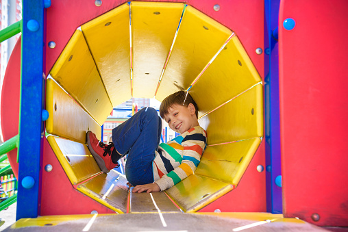 Happy little boy playing in tube or tunnel at the modern playground. Summer holidays. Happy and healthy childhood.