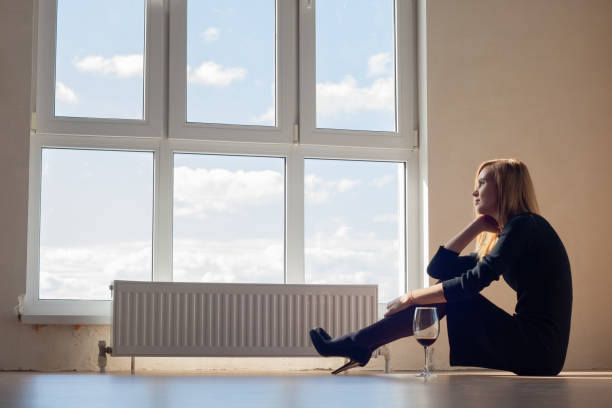 upset girl in an empty room sitting on the floor with a glass of wine - eastern european caucasian one person alcoholism imagens e fotografias de stock