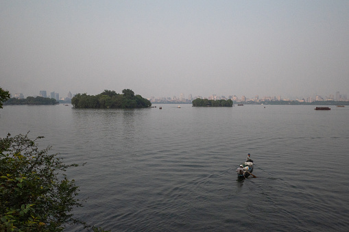 Hangzhou, China - 10 May 2019: Traditional boat over West Lake with skyline of the city center