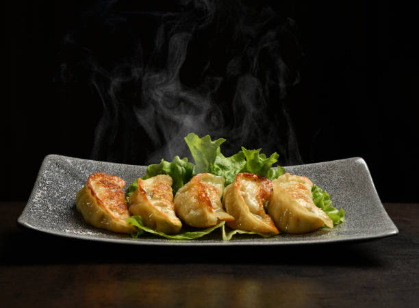 Japanese fried dumplings - Gyoza with pork meat and vegetables served on a plate with steam smoke Japanese fried dumplings - Gyoza with pork meat and vegetables served on a plate with steam smoke on black background chinese dumpling photos stock pictures, royalty-free photos & images