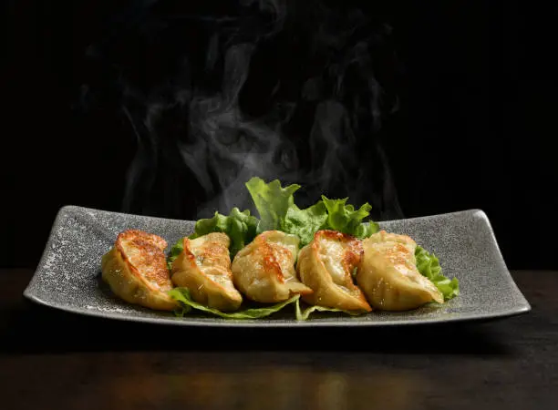 Japanese fried dumplings - Gyoza with pork meat and vegetables served on a plate with steam smoke on black background