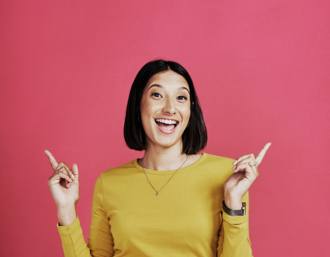 Cropped portrait of an attractive young woman standing and making a hand gesture against a pink background in the studio