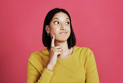 Cropped shot of an attractive young woman standing alone and looking contemplative against a pink background in the studio