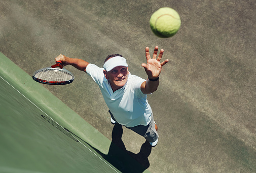 High angle shot of a focused middle aged man playing tennis while about to serve the ball to his opponent outside during the day