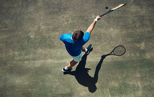 High angle shot of a focused young man playing tennis outside on a tennis court during the day