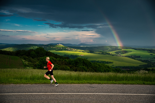 Athlete train in summer green landscape, rainbow in background
