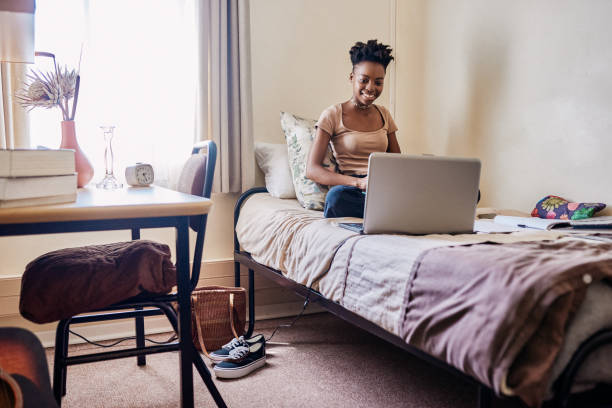 Studying is a cruise when you love your majors Shot of an attractive young female university student using a laptop while studying in her room college dorm photos stock pictures, royalty-free photos & images