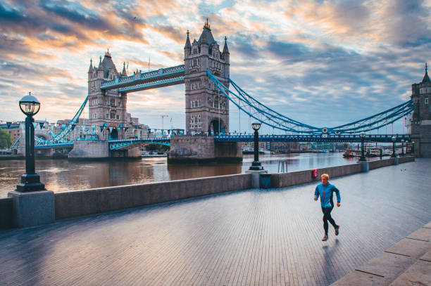 コロナウイルス、covid-19検疫時間のロンドンの空の通りで一人ランナー。背景にタワーブリッジ - tower bridge uk london england people ストックフォトと画像