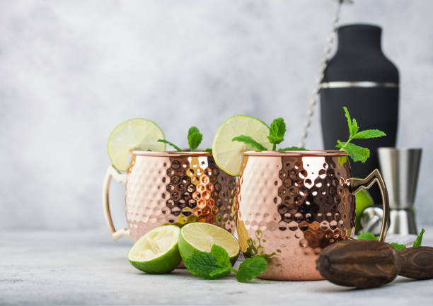 istock Moscow mule cocktail in a copper mug with lime and mint and wooden squeezer on light background with black shaker and jigger 1215930024