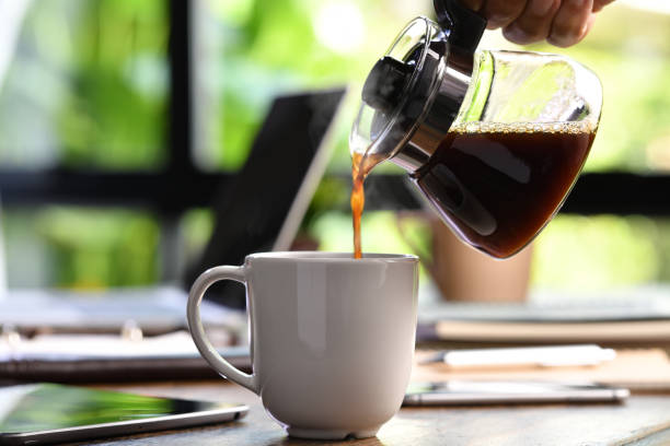uma mão derramando café fumegante em uma xícara em uma mesa de trabalho quando o trabalho de casa - cafe laptop espresso business - fotografias e filmes do acervo