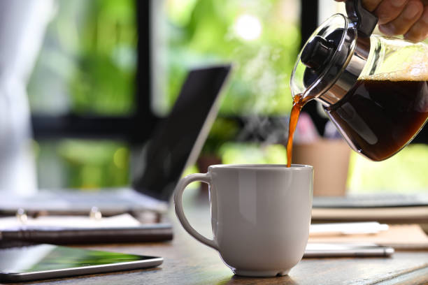 una mano vertiendo café al vapor en una taza en un escritorio cuando trabajas desde casa - cafe laptop espresso business fotografías e imágenes de stock