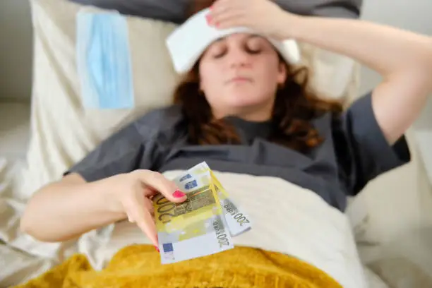 Woman holds out money for treatment while lying in bed. The patient pays for medical services in euro bills