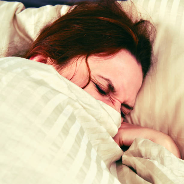 istock A woman with a coronavirus is covered with a blanket and squints while lying on the bed 1215933339